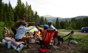 friends camping and drinking out of mugs in front of a bonfire